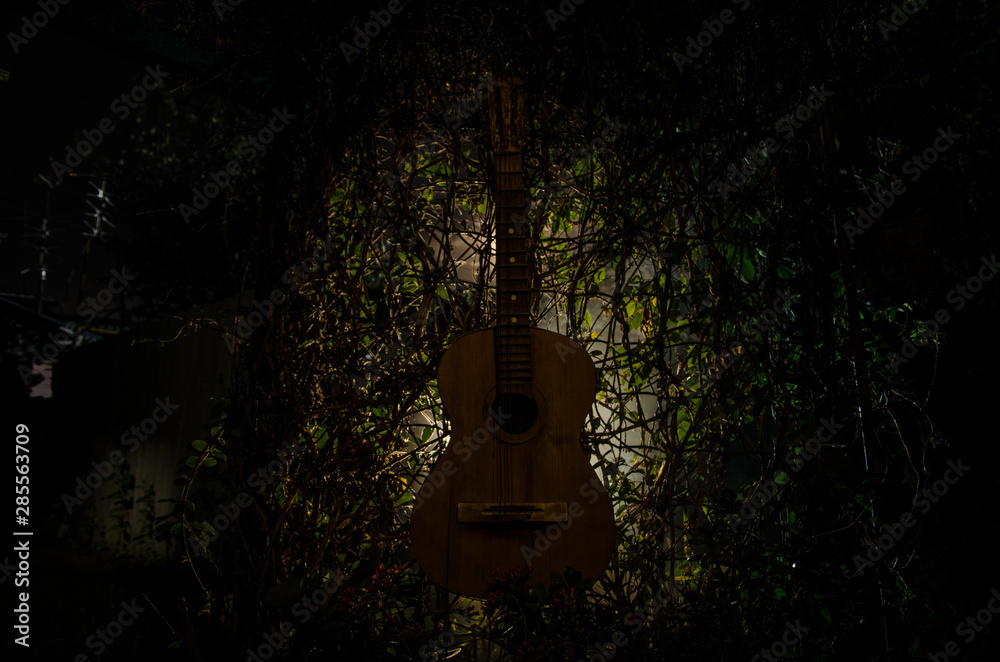 Fototapeta An wooden acoustic guitar is against a grunge textured wall. The room is dark with a spotlight for your copyspace.