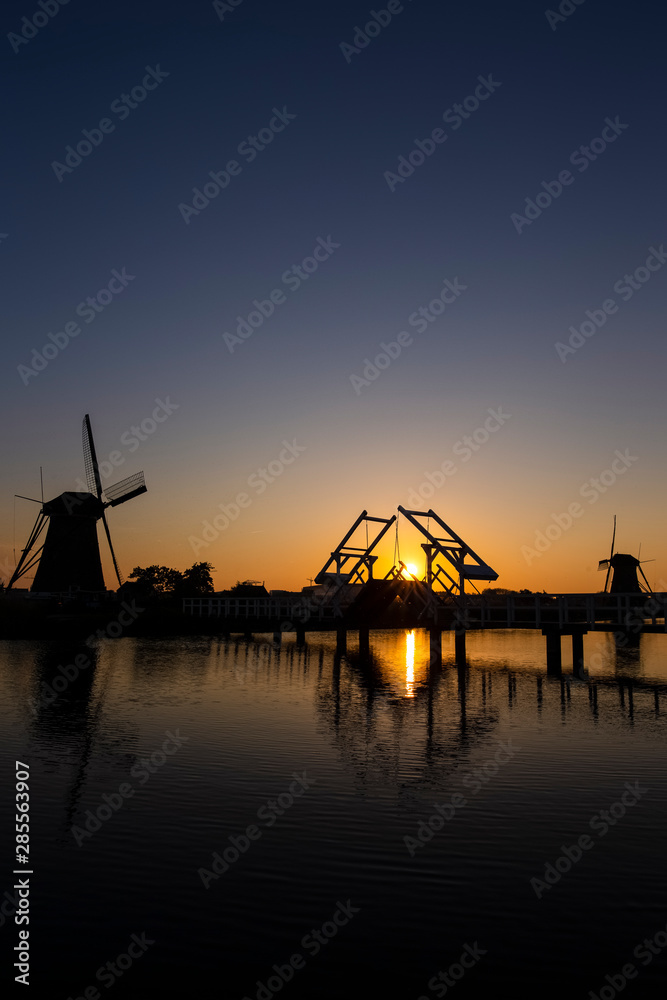 Traditional Romantic Dutch Windmills and Wooden Drawbridge in Kinderdijk Village in the Netherlands. Picture Taken At Golden Hour.