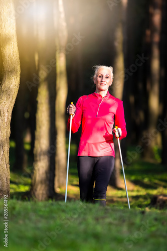 Smiling Mature Adult Caucasian Woman Nodic Trekking in Summer Forest Outdoors. photo