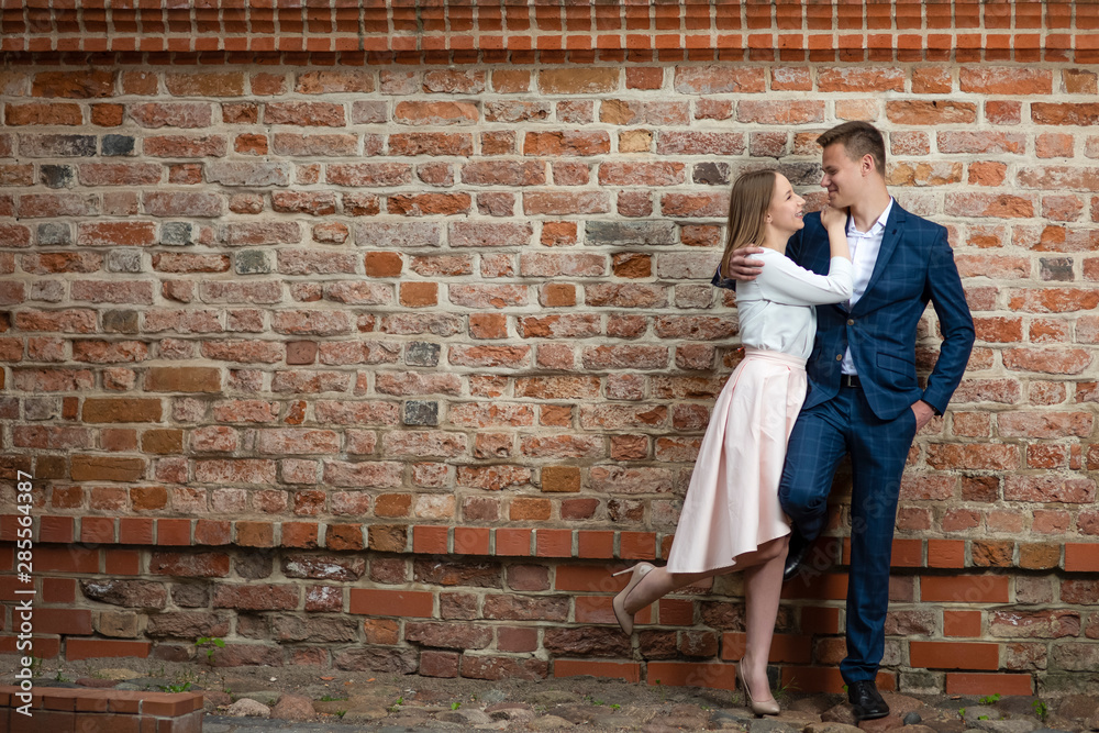 Portrait of Smiling Happy Couple Embracing Together Against Brick Wall.