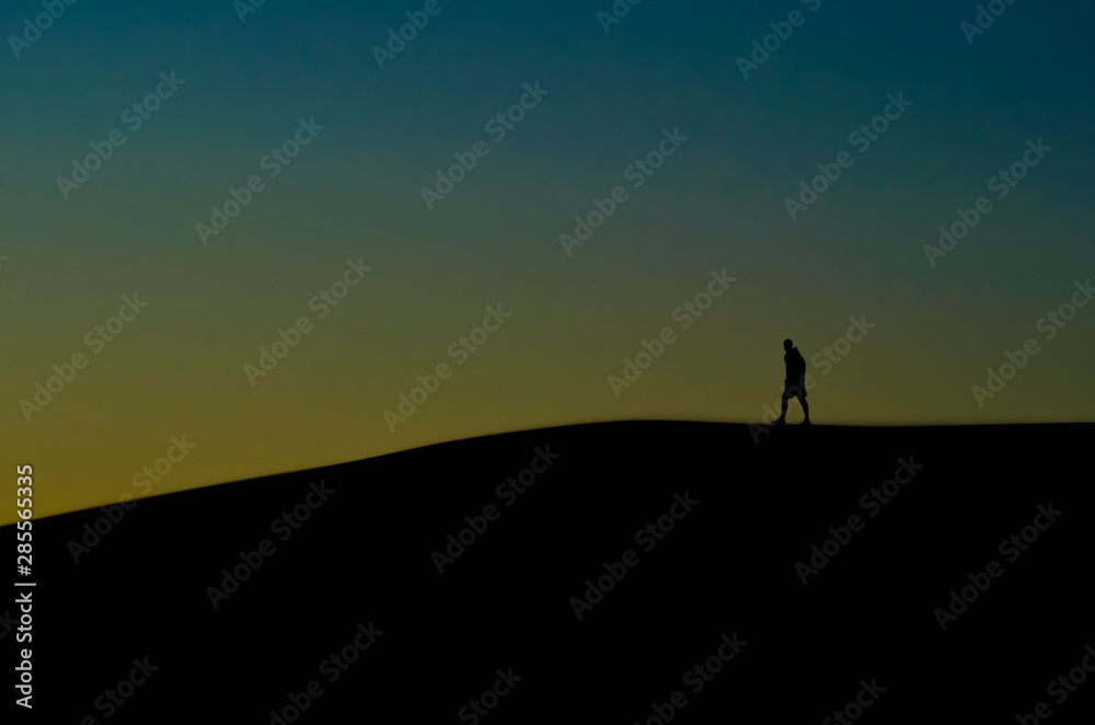 Silhouettes of man walking through dunes