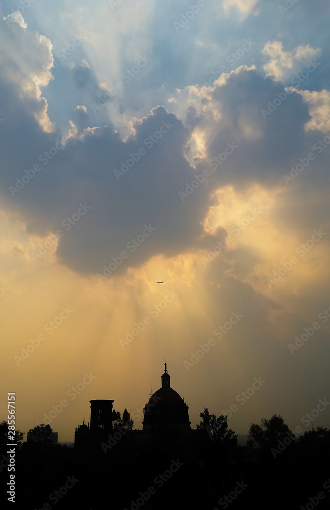 plane passing flying over a building church and the clouds with a ray of light