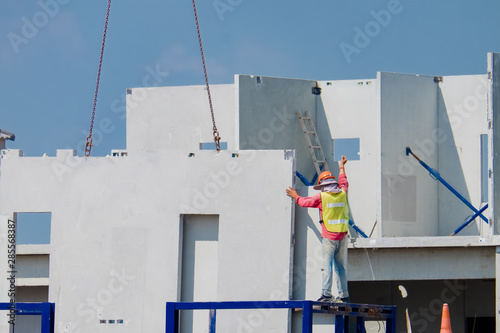 Construction worker are installing the precast concrete wall, orange safety helmet and green vest.