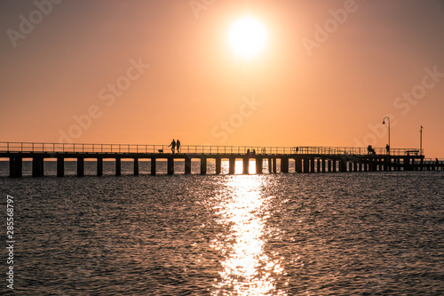 Couple walking their dog on a pier silhouettes at sunset