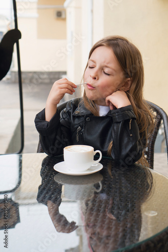 Stylish little schoolgirl enjoys delicious coffee on the summer terrace of the restaurant. Coffee break. photo