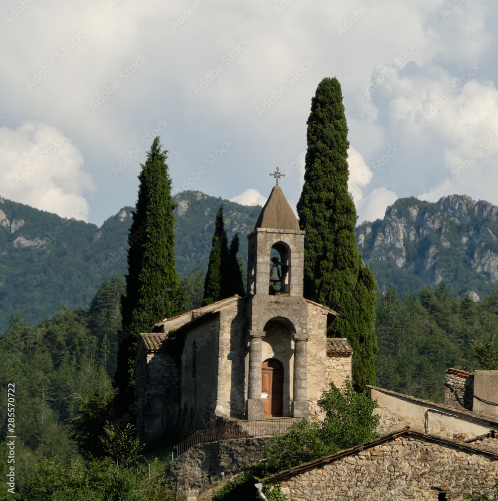 The church of St-Benoit-en-Diois with cedar trees and mountains in the Drome region of France The church of St-Benoit-en-Diois with cedar trees and mountains in the Drome region of France