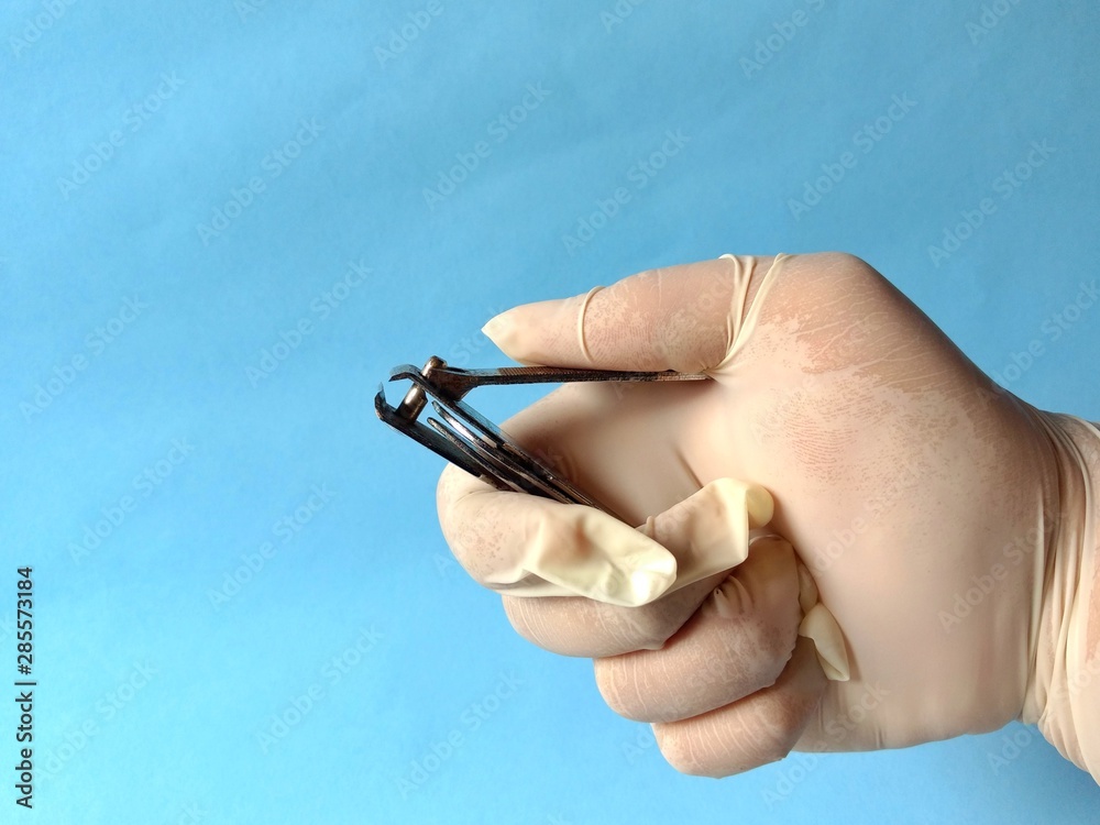 Hand with white glove holding a nail clipper to care for a patient. medical concept Hand with white glove holding a nail clipper to care for a patient. medical concept