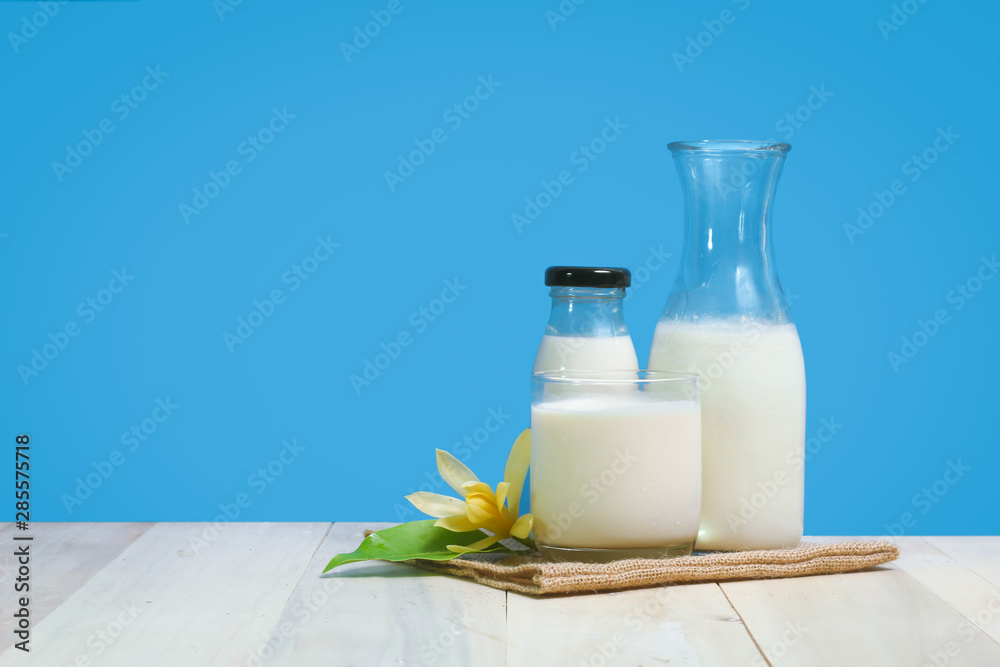 A bottle of rustic milk and glass of milk on a wooden table on a blue background A bottle of rustic milk and glass of milk on a wooden table on a blue background