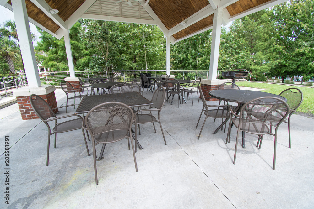 An empty pavilion filled with outdoor metal park tables and chairs during a sunny day outside 