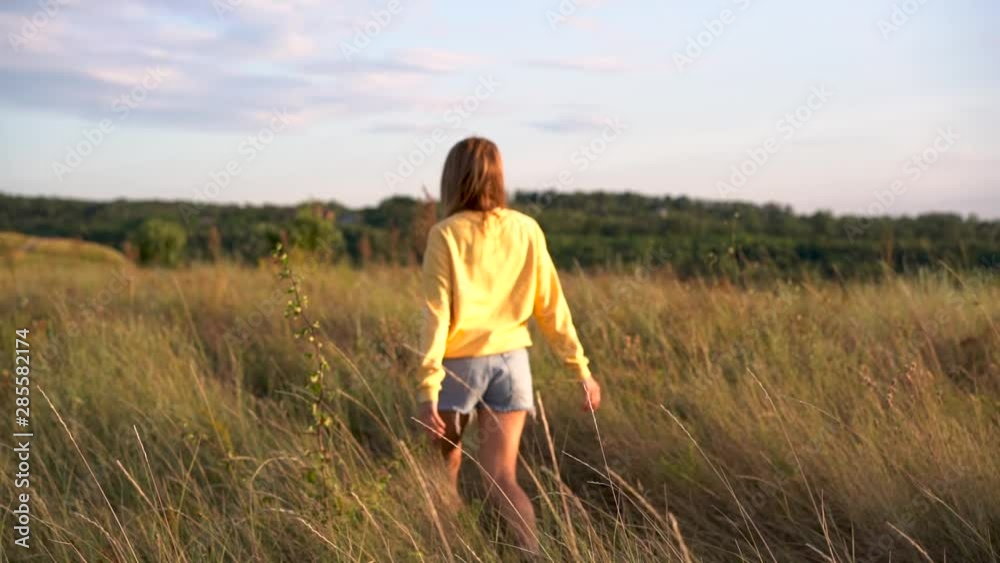 Young woman walking in a field, touching yellow grass Young woman walking in a field, touching yellow grass