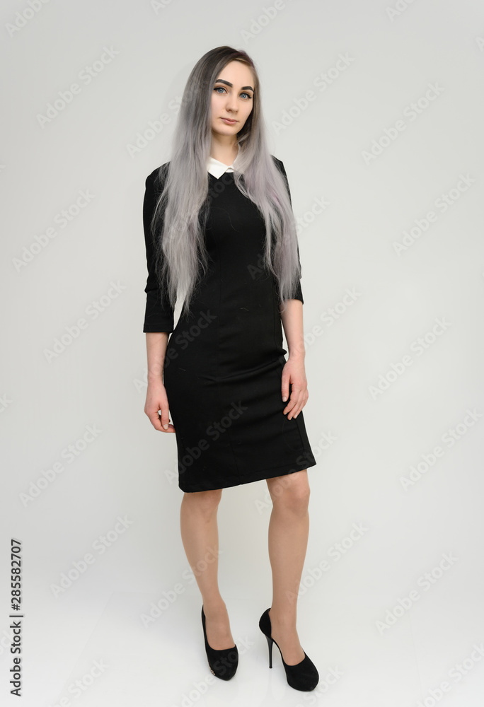 Full length studio portrait of a pretty manager girl with long beautiful hair in a black dress on a white background. He stands in front of the camera, smiles, shows his hands. Full length studio portrait of a pretty manager girl with long beautiful hair in a black dress on a white background. He stands in front of the camera, smiles, shows his hands.