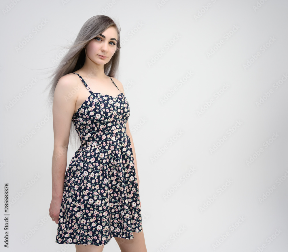 Studio portrait of a knee-length of a pretty student girl with long beautiful hair in a beautiful color dress on a white background. He stands straight, smiles, shows with his hands. Studio portrait of a knee-length of a pretty student girl with long beautiful hair in a beautiful color dress on a white background. He stands straight, smiles, shows with his hands.