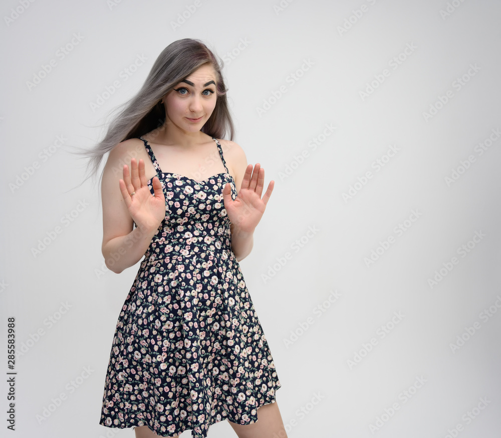 Studio portrait of a knee-length of a pretty student girl with long beautiful hair in a beautiful color dress on a white background. He stands straight, smiles, shows with his hands. Studio portrait of a knee-length of a pretty student girl with long beautiful hair in a beautiful color dress on a white background. He stands straight, smiles, shows with his hands.