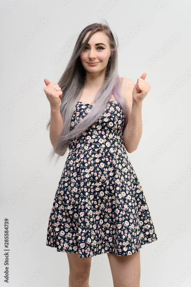 Full length studio portrait of a pretty student girl with long beautiful hair in a beautiful color dress on a white background. He stands straight, smiles, shows with his hands. Full length studio portrait of a pretty student girl with long beautiful hair in a beautiful color dress on a white background. He stands straight, smiles, shows with his hands.