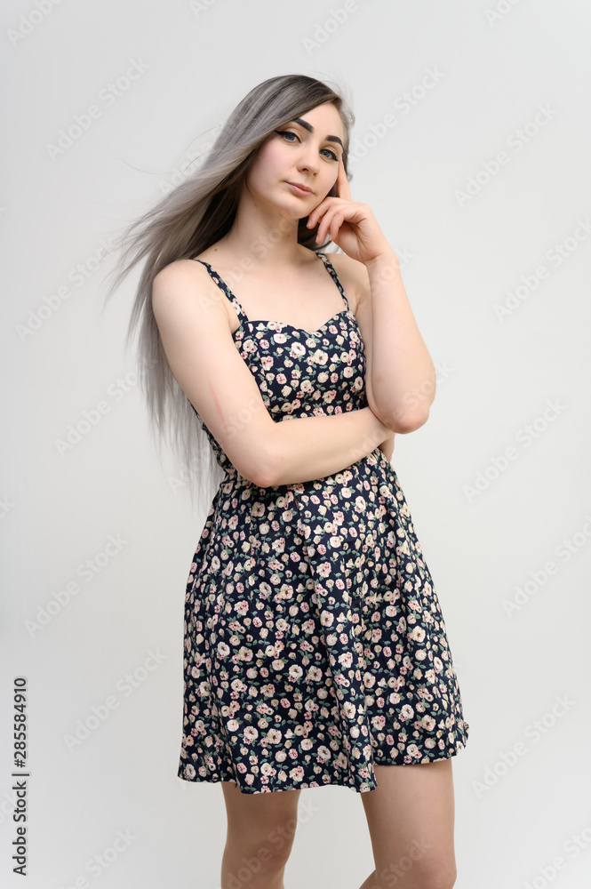 Full length studio portrait of a pretty student girl with long beautiful hair in a beautiful color dress on a white background. He stands straight, smiles, shows with his hands. Full length studio portrait of a pretty student girl with long beautiful hair in a beautiful color dress on a white background. He stands straight, smiles, shows with his hands.
