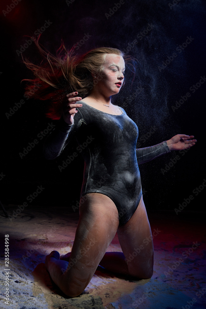 Young teen girl in a dark room during a photoshoot with flour with a colored light and a black background