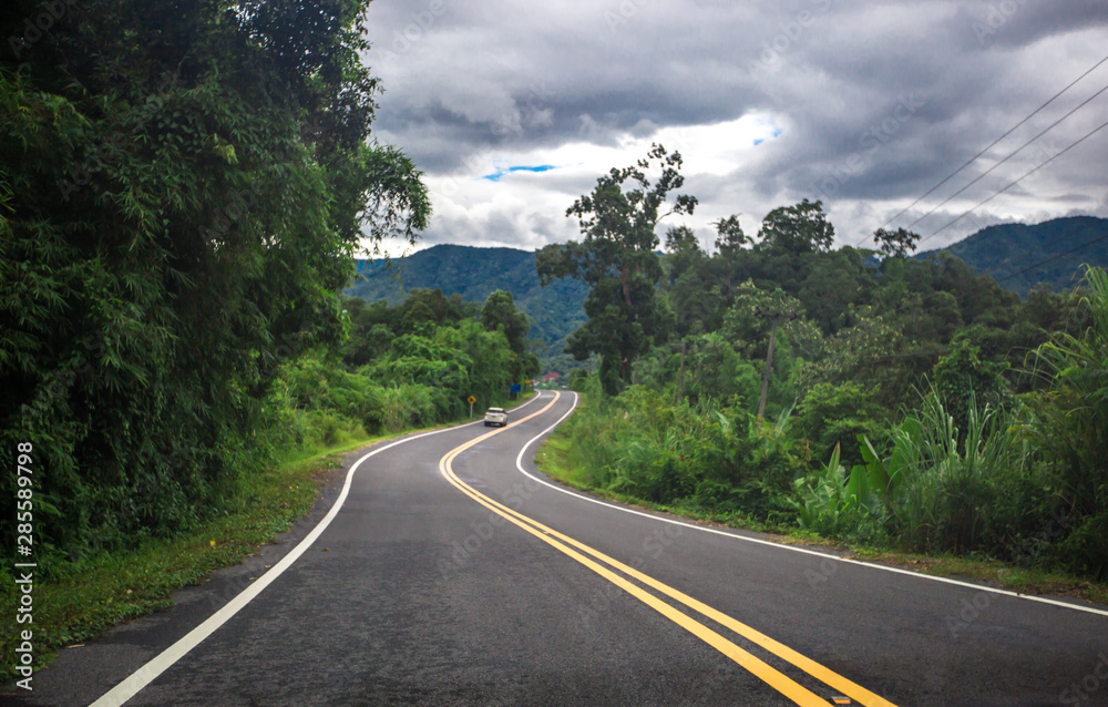 Blurred background of a mountain road view, from a car windscreen that runs with care, with natural scenery surrounded by plants, large trees Blurred background of a mountain road view, from a car windscreen that runs with care, with natural scenery surrounded by plants, large trees