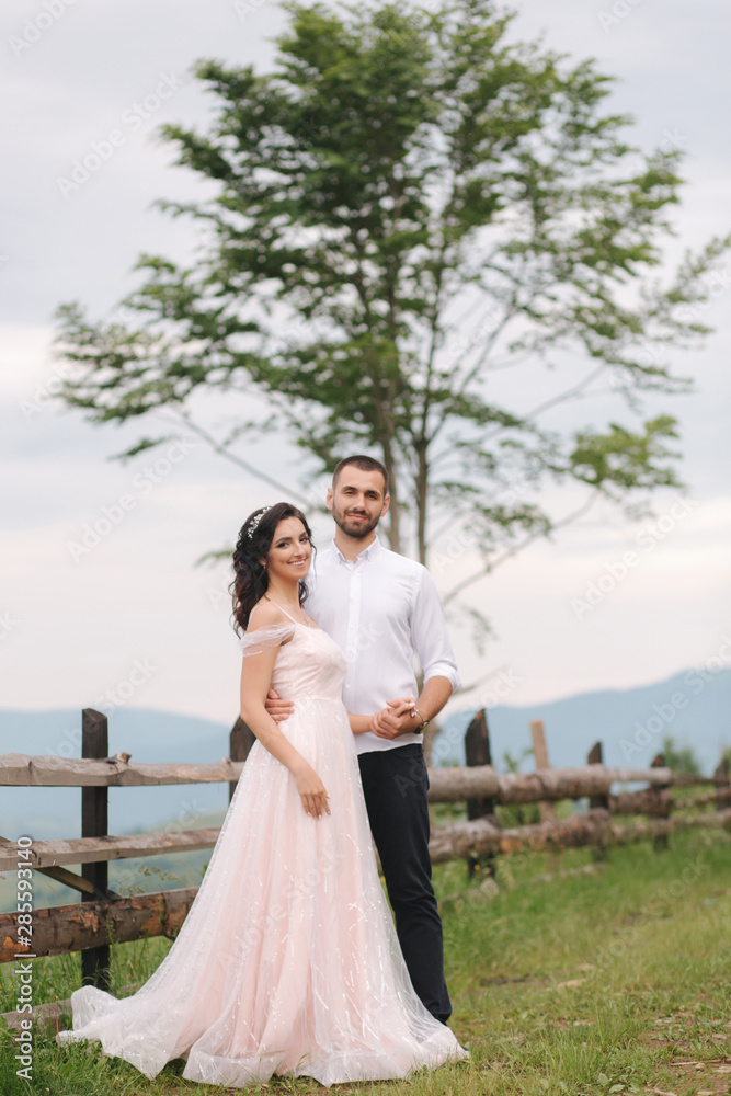 Lovestory of beautiful couple in the mountains, Handsome bearded man with beautiful and charming woman. Couple stand in front of beautiful tree