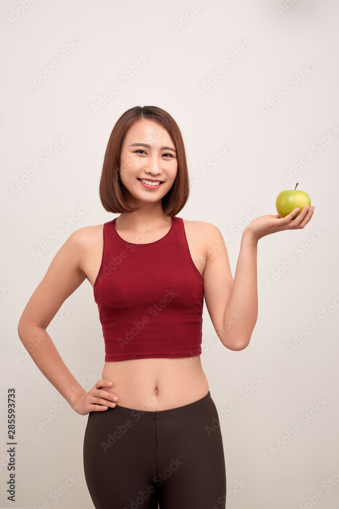 Fitness woman eating apple wearing measuring tape. Fit sporty multicultural Asian / Caucasian female fitness woman isolated on white background. - Image Fitness woman eating apple wearing measuring tape. Fit sporty multicultural Asian / Caucasian female fitness woman isolated on white background. - Image