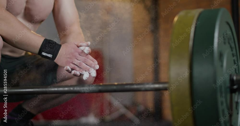 Young muscular man in Gym, clapping hands with white chalk, white particles and dust fly in air, slow motion, crossfit training day. Young muscular man in Gym, clapping hands with white chalk, white particles and dust fly in air, slow motion, crossfit training day.