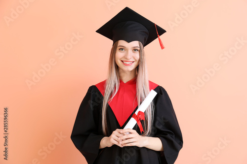 Obraz na plátne Young female student in bachelor robe and with diploma on color background