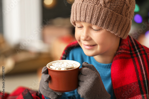 Fototapeta Cute little boy drinking hot chocolate at home on Christmas eve