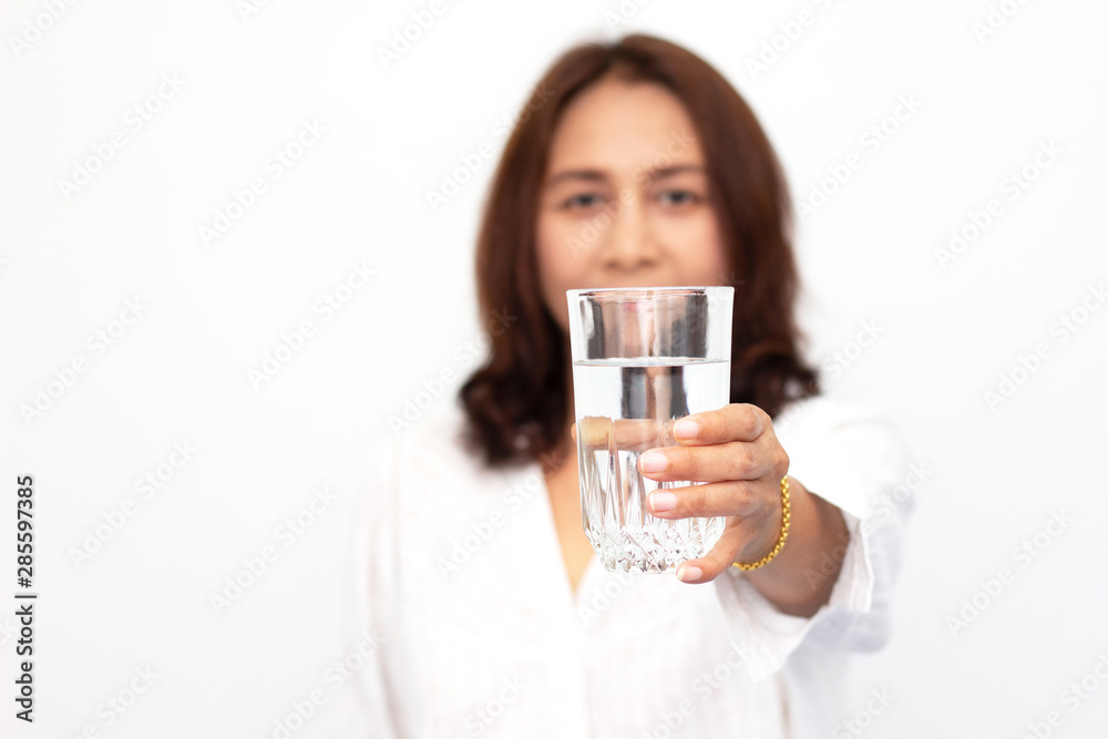 Happy young woman showing drinking glass with water at home.Focus on the glass Happy young woman showing drinking glass with water at home.Focus on the glass