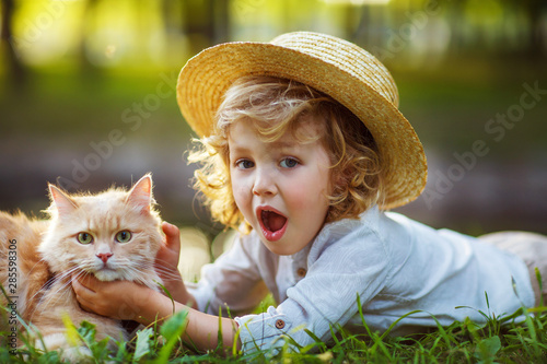 Little curly boy with a redhead cat, outdoor summer day