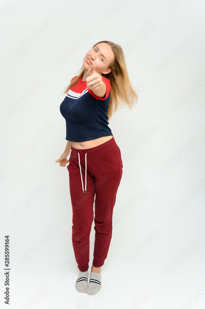 Full length studio portrait of a pretty young happy blonde woman in a tracksuit on a white background. He smiles, talks, shows with his hands, moves, shows emotions. Full length studio portrait of a pretty young happy blonde woman in a tracksuit on a white background. He smiles, talks, shows with his hands, moves, shows emotions.