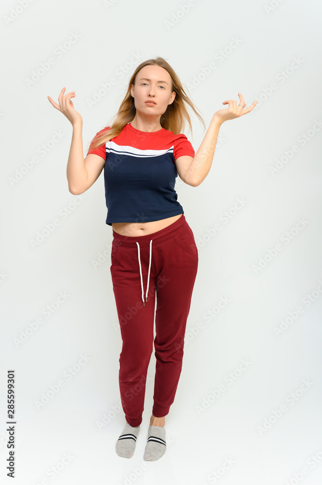 Full length studio portrait of a pretty young happy blonde woman in a tracksuit on a white background. He smiles, talks, shows with his hands, moves, shows emotions. Full length studio portrait of a pretty young happy blonde woman in a tracksuit on a white background. He smiles, talks, shows with his hands, moves, shows emotions.