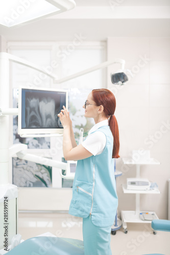 Red-haired dentist with ponytail studying X-ray of patient