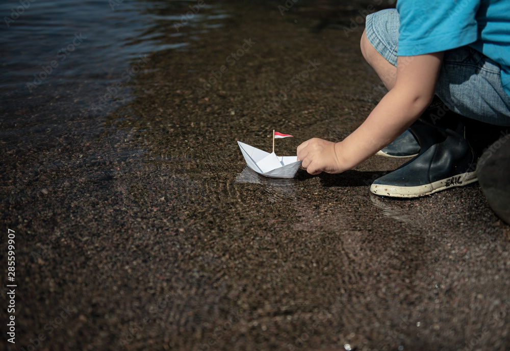 Kleiner Junge setzt Papierschiff ins Wasser Kleiner Junge setzt Papierschiff ins Wasser