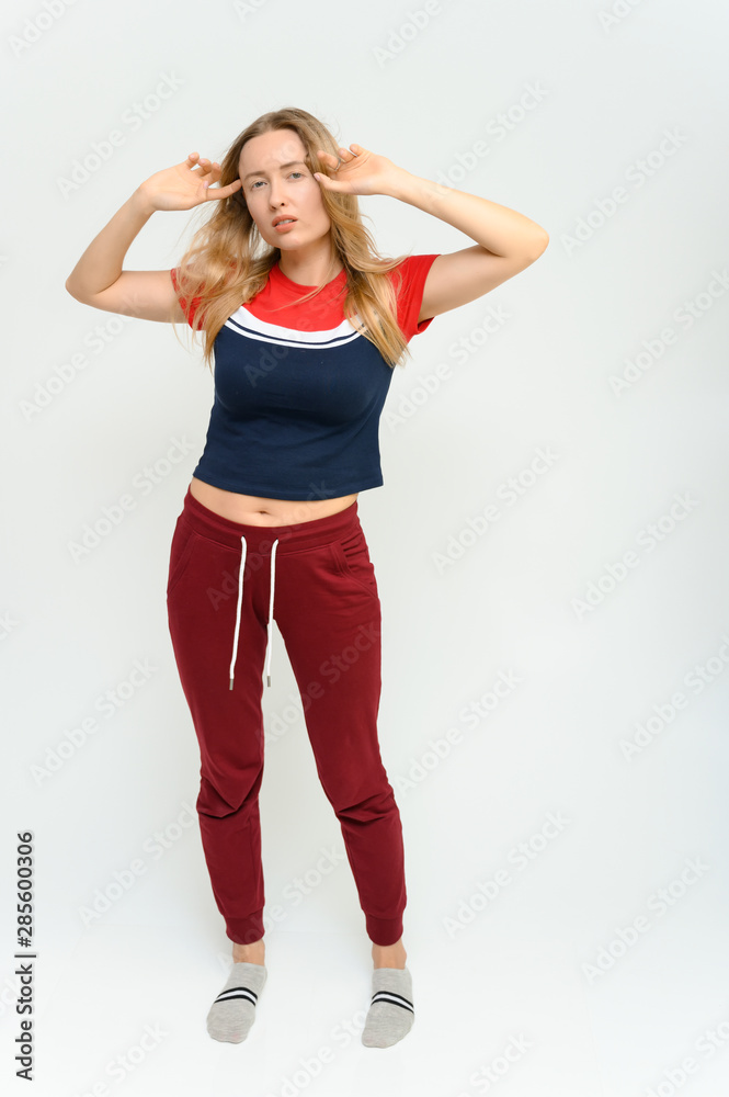 Full length studio portrait of a pretty young happy blonde woman in a tracksuit on a white background. He smiles, talks, shows with his hands, moves, shows emotions. Full length studio portrait of a pretty young happy blonde woman in a tracksuit on a white background. He smiles, talks, shows with his hands, moves, shows emotions.