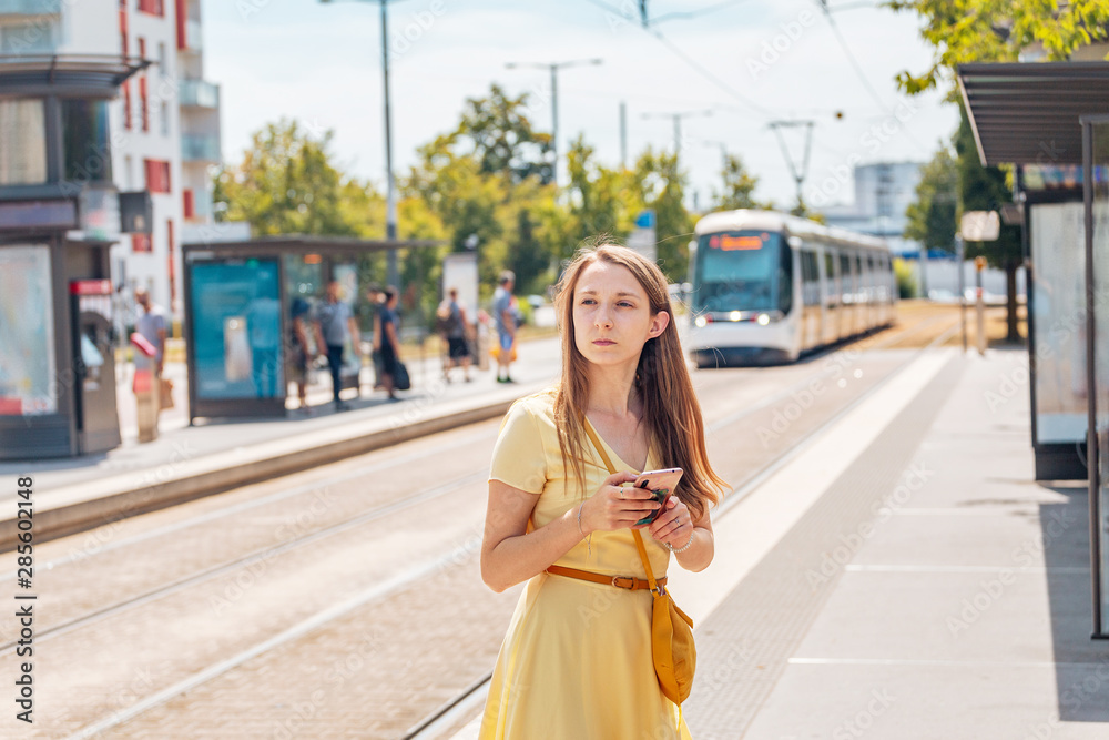 A frustrated girl with a smartphone waiting for a delayed tram.
