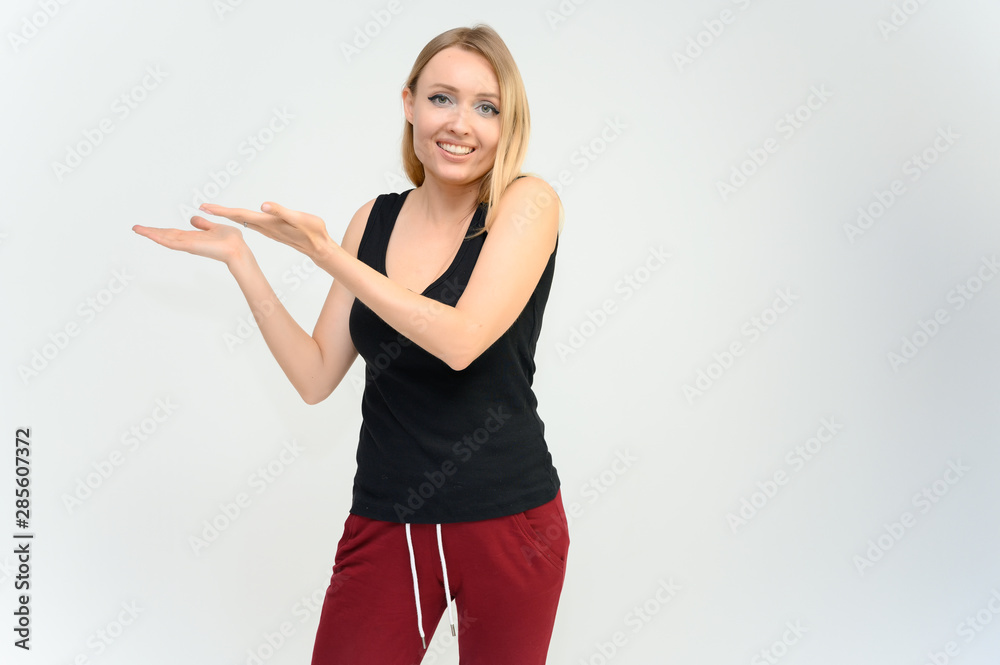 Studio knee-length portrait of a pretty beautiful young happy blonde woman on a white background in a black t-shirt and red trousers. Smiling, talking, showing emotions. Studio knee-length portrait of a pretty beautiful young happy blonde woman on a white background in a black t-shirt and red trousers. Smiling, talking, showing emotions.