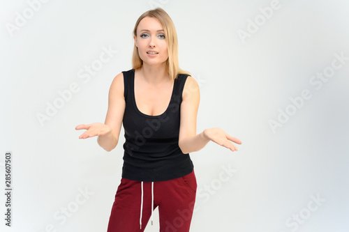 Studio knee-length portrait of a pretty beautiful young happy blonde woman on a white background in a black t-shirt and red trousers. Smiling, talking, showing emotions. © Вячеслав Чичаев