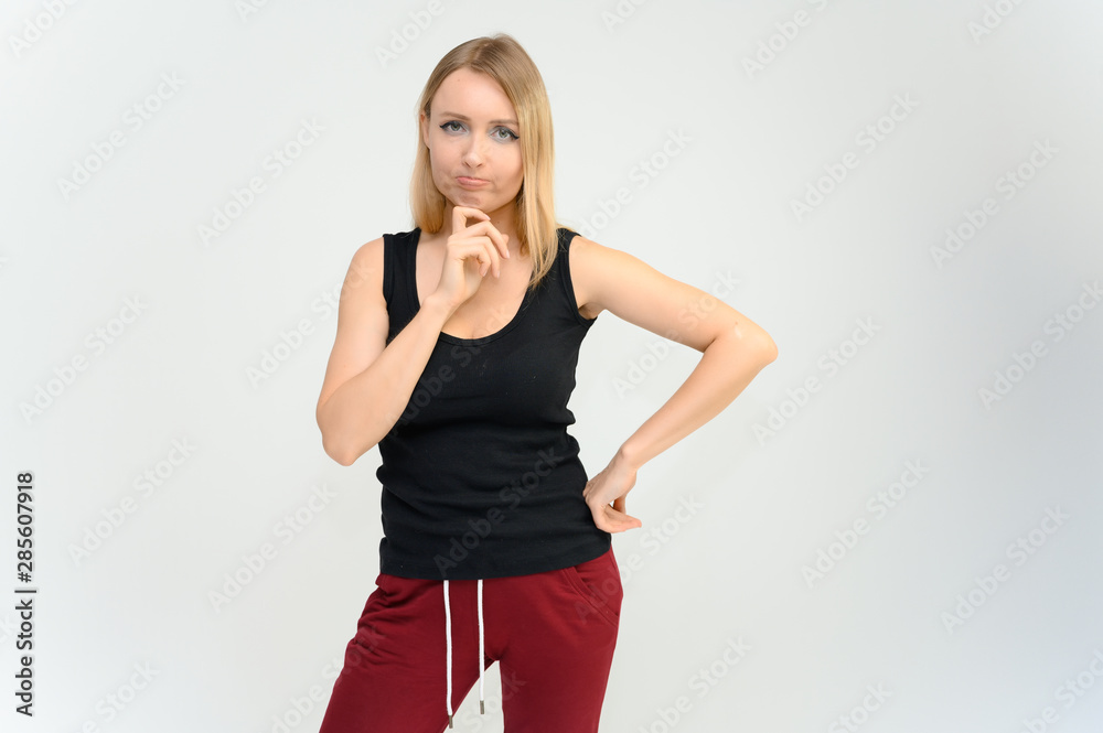 Studio knee-length portrait of a pretty beautiful young happy blonde woman on a white background in a black t-shirt and red trousers. Smiling, talking, showing emotions. Studio knee-length portrait of a pretty beautiful young happy blonde woman on a white background in a black t-shirt and red trousers. Smiling, talking, showing emotions.