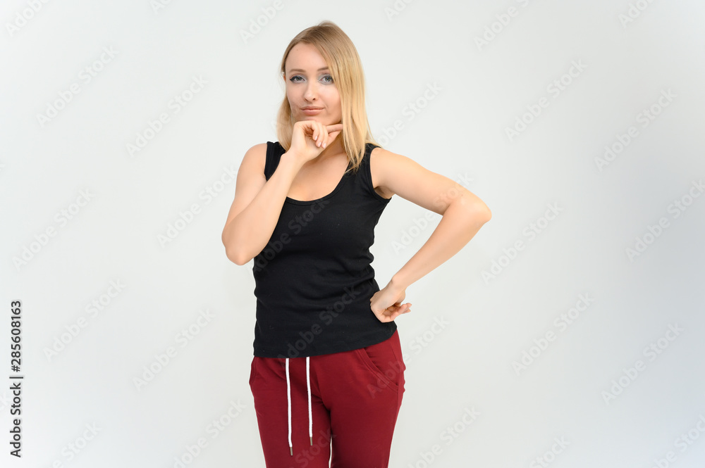 Studio knee-length portrait of a pretty beautiful young happy blonde woman on a white background in a black t-shirt and red trousers. Smiling, talking, showing emotions. Studio knee-length portrait of a pretty beautiful young happy blonde woman on a white background in a black t-shirt and red trousers. Smiling, talking, showing emotions.