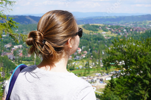 girl of European appearance looks through dark glasses at mountains on Sunny summer day. brown-haired woman with tied hair, traveler with backpack