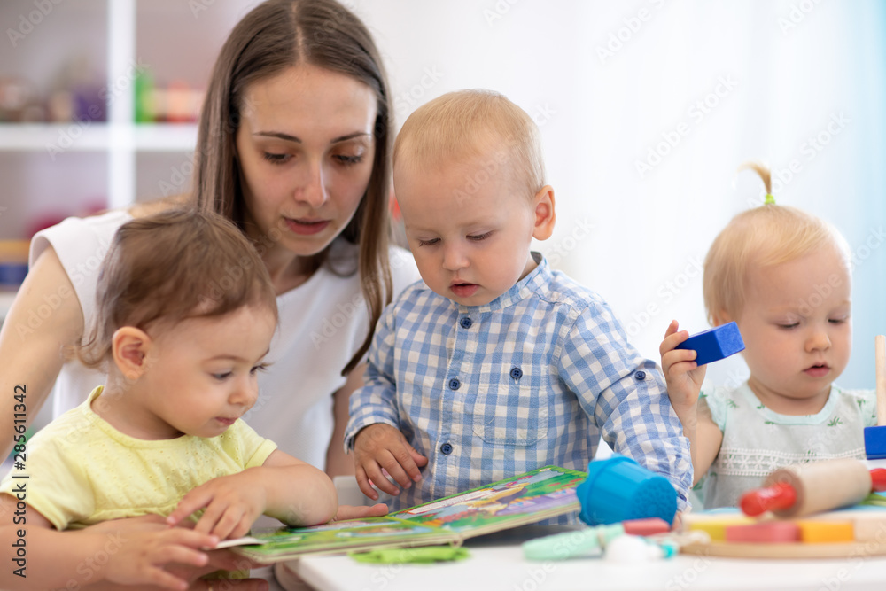 Kindergarten teacher reads book to kids in nursery. Lesson for babies in creche Kindergarten teacher reads book to kids in nursery. Lesson for babies in creche