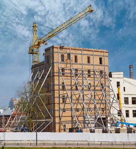 Building with reinforced wall and crane on construction site. Strengthening old brick wall structure. Bolting vertical channel-section steel girders. Renovation and restavration of old building facade photo