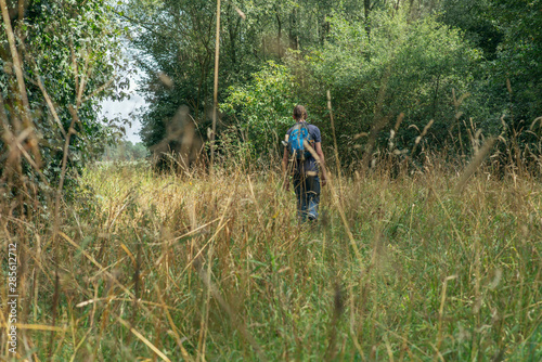 Man with backpack hikes through forest field in summer.