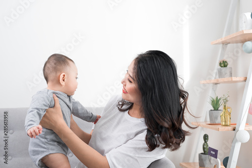 Young mother with her one years old little son dressed in pajamas are relaxing and playing in the living room at the weekend together, lazy morning, warm and cozy scene. Selective focus.