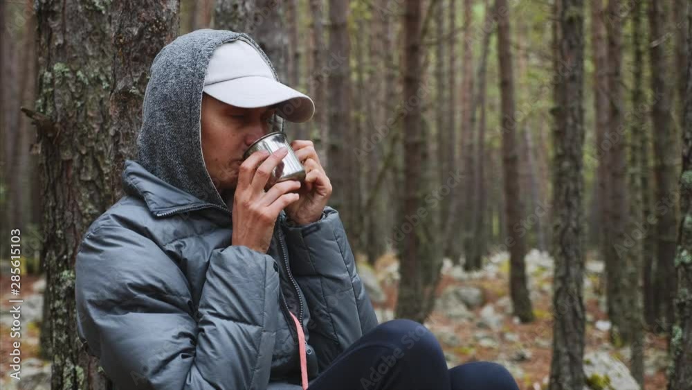 Woman hiker on nature camping in pine wood. Portrait of young woman traveller drinking tea from metal cup sitting in forest. She is resting on nature enjoying her vacation. Travel and hiking concept. Woman hiker on nature camping in pine wood. Portrait of young woman traveller drinking tea from metal cup sitting in forest. She is resting on nature enjoying her vacation. Travel and hiking concept.
