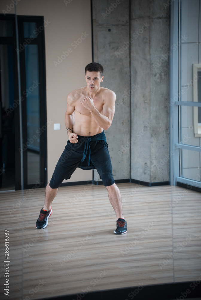 An athletic man boxer standing in fighting pose in the bright studio - training