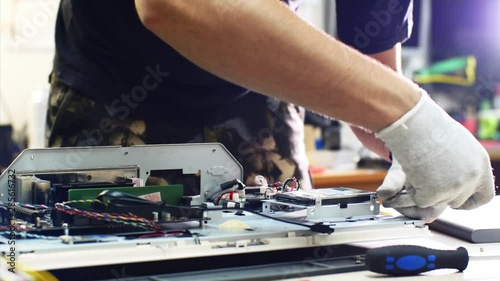 Computer hard drive ssd upgrade, diagnosing breakdowns. Technician detaches hard drive from monoblock repairing it in service center workshop, hands closeup. He unscrews computer details screwdriver. photo