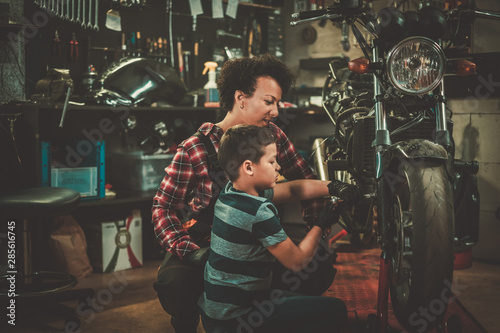 African american woman mechanic and boy helper repairing a motorcycle in a workshop