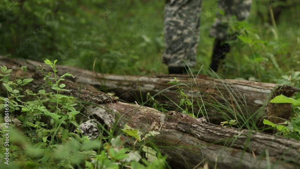Close-up of legs stepping over a log in the forest, a man in camouflage clothes and black army boots Close-up of legs stepping over a log in the forest, a man in camouflage clothes and black army boots