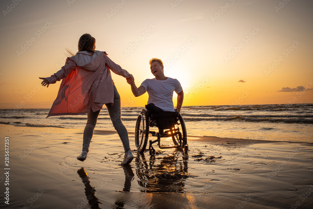 Handicapped man in wheelchair and his girlfriend on a beach at sunset ...