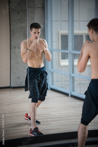 An athletic man standing in the studio - training in front of the mirror